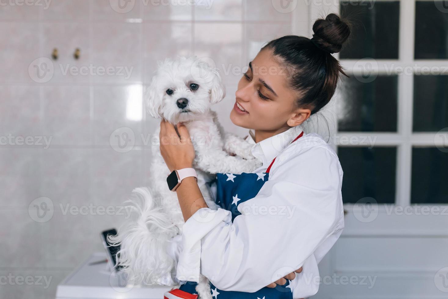 Smiling woman in kitchen holding cute white Maltese dog photo