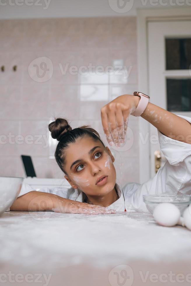 Tired young woman is pouring flour on the kitchen table photo