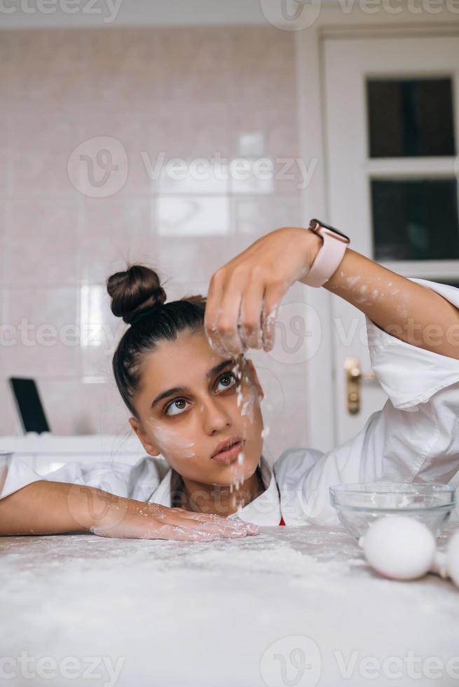 una joven cansada está vertiendo harina en la mesa de la cocina foto