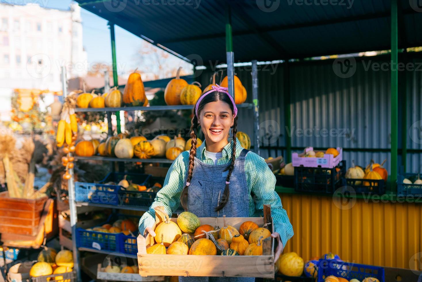 Farmer woman holds a wooden box with pumpkins in hands photo