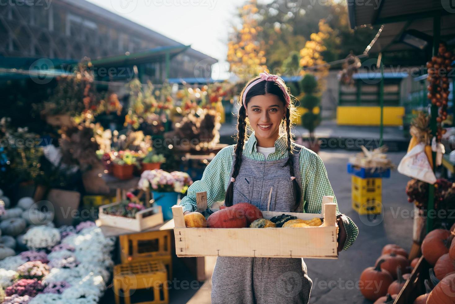 Farmer woman holds a wooden box with pumpkins in hands photo