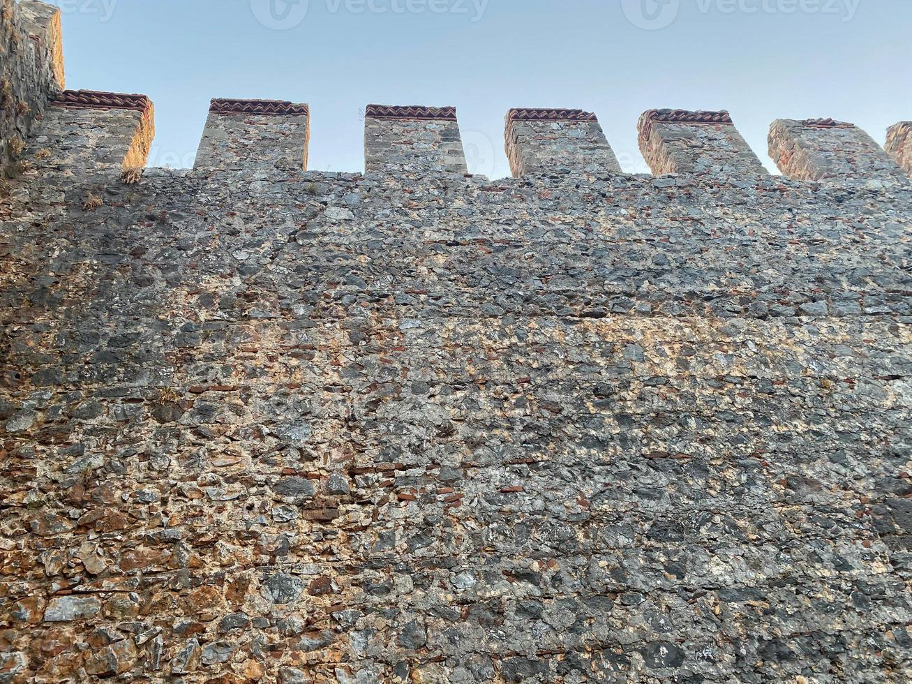 Large stone wall of an old ancient medieval fortress made of cobblestones against a blue sky photo