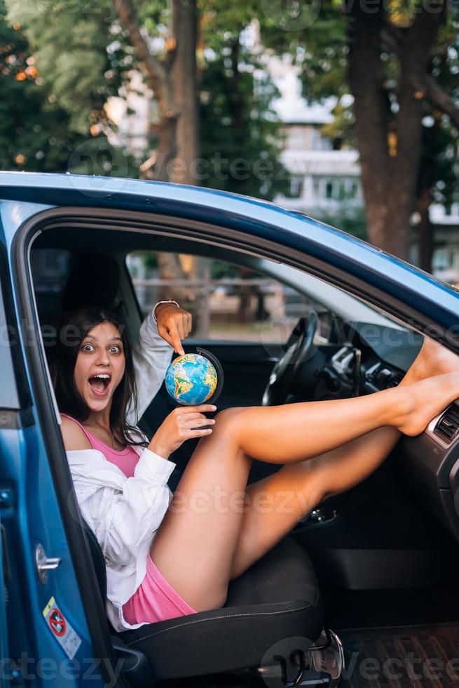 Young woman sitting in a car and holding a globe photo