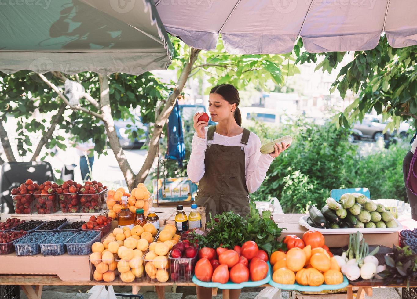 Young saleswoman holding zucchini and tomato in hands photo