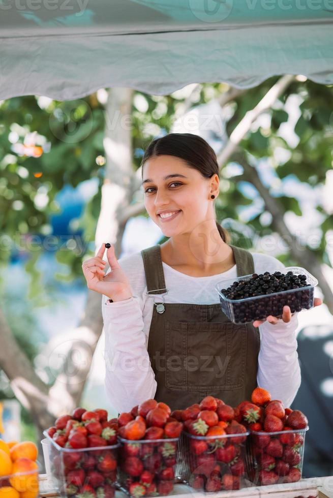 Young positive saleswoman at work, holding currants in her hands photo