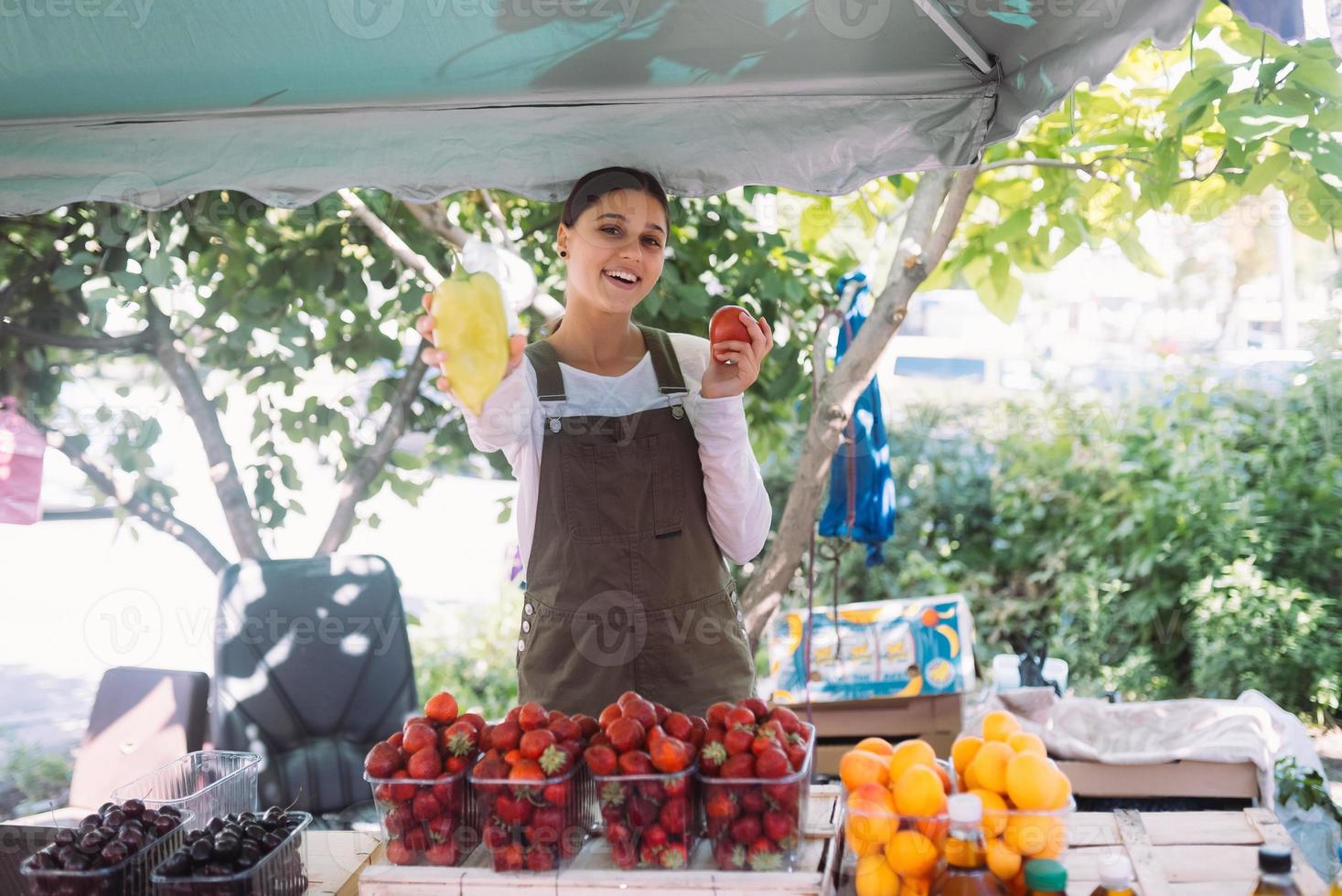 Young saleswoman holding bell pepper and tomato in hands photo