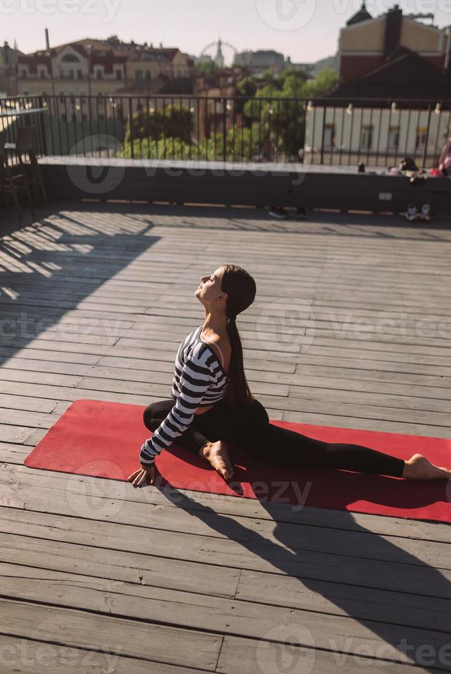 Woman doing yoga exercises on house roof in early morning photo