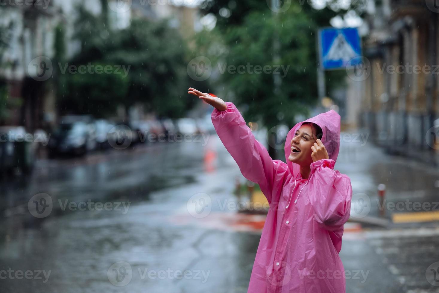 joven mujer sonriente con impermeable mientras disfruta de un día lluvioso. foto