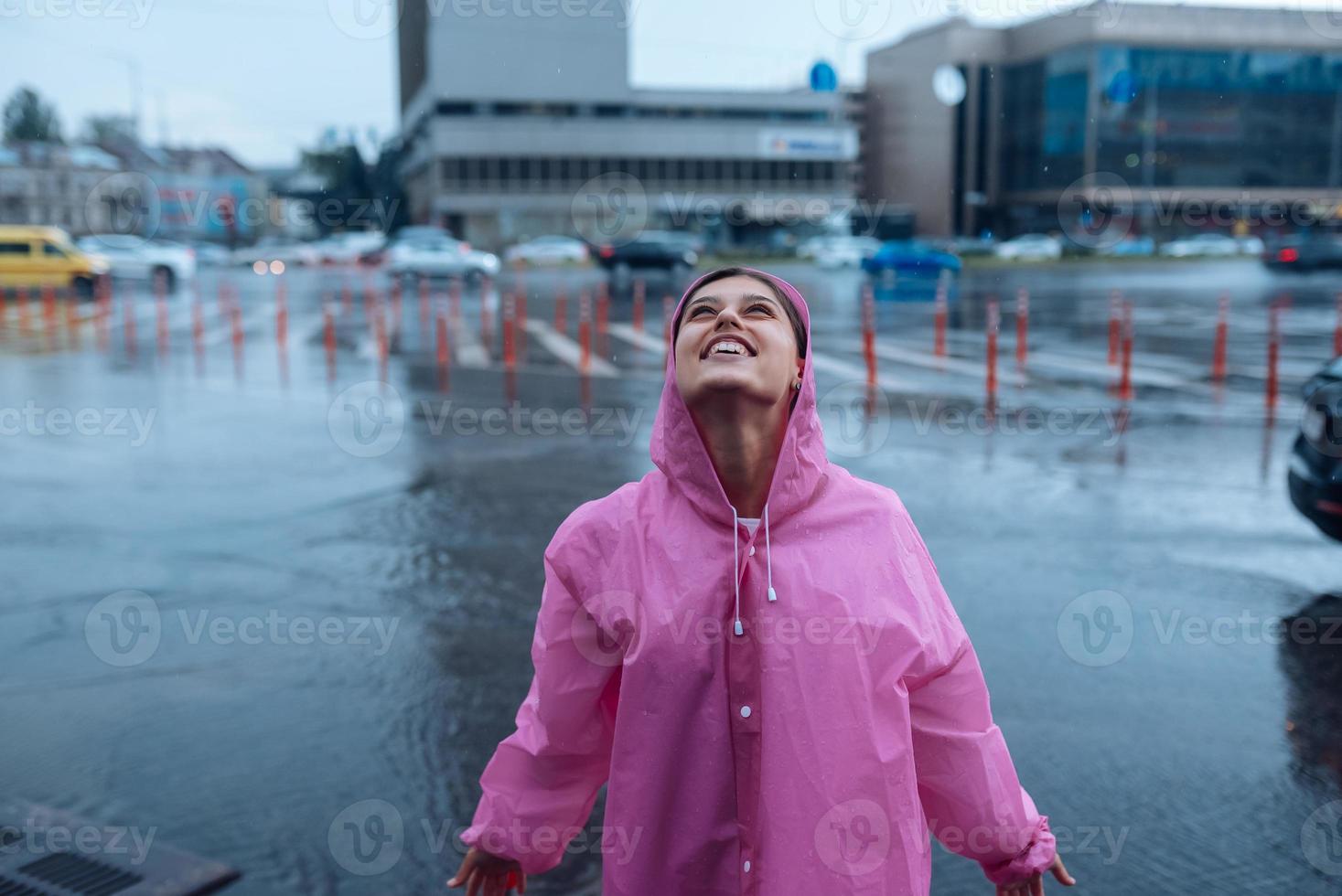 Young smiling woman in a pink raincoat enjoying a rainy day. photo