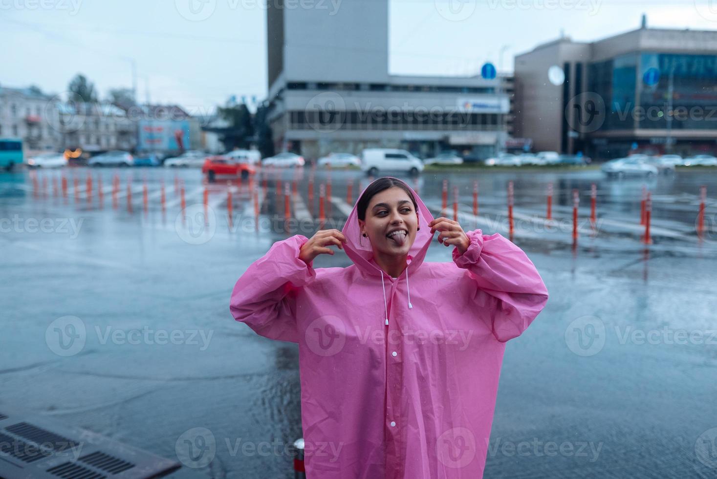 joven mujer sonriente con un impermeable rosa disfrutando de un día lluvioso. foto