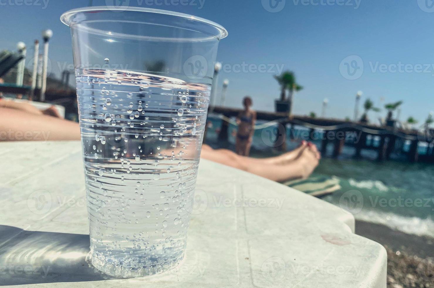 a plastic glass is on the table, a transparent carbonated drink is poured inside. relaxing on the beach, cooling the body with drinks. body water photo