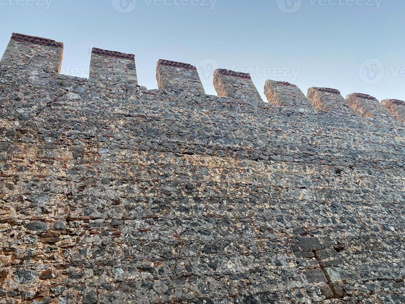 Large stone wall of an old ancient medieval fortress made of cobblestones against a blue sky photo