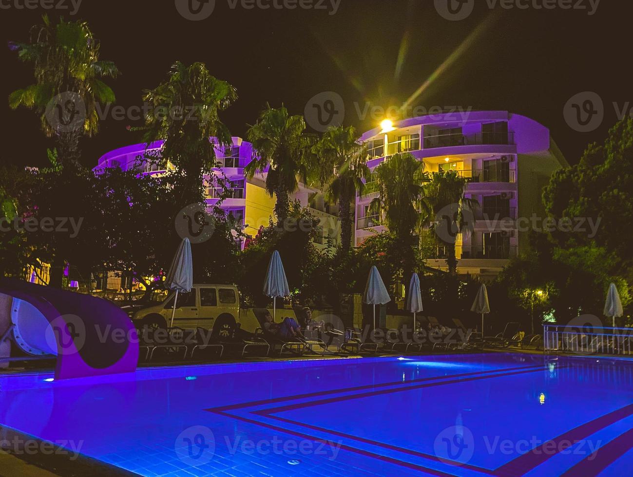 beach for tourists, swimming pool and bar near the hotel. near the water there are folded white umbrellas, slides for riding into the water. relaxing by the pool, traveling photo