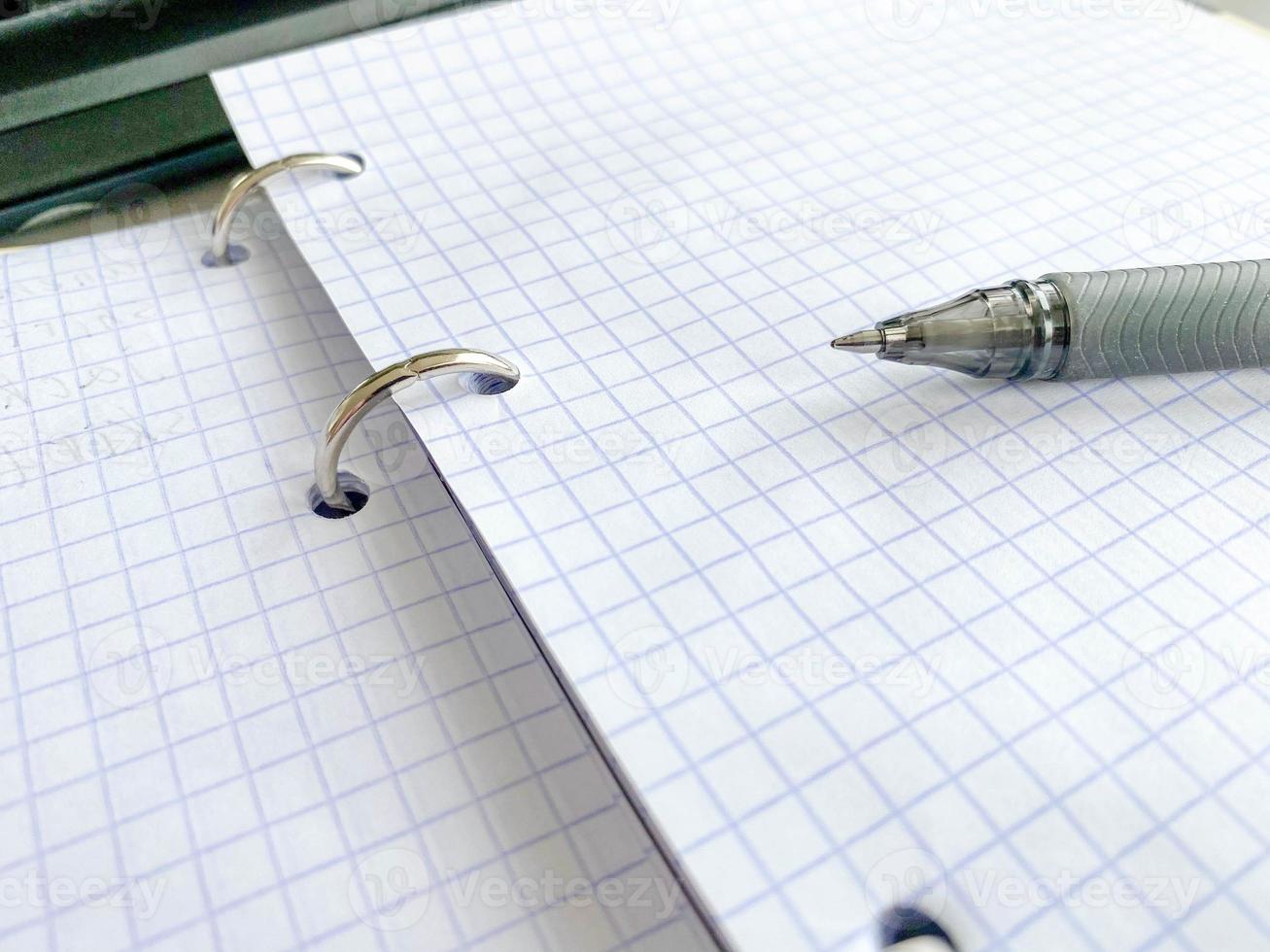 on the table lies a notepad for notes on paper clips in small cells. records for work. on the pages is a pen with a blue rod and a thin lead photo