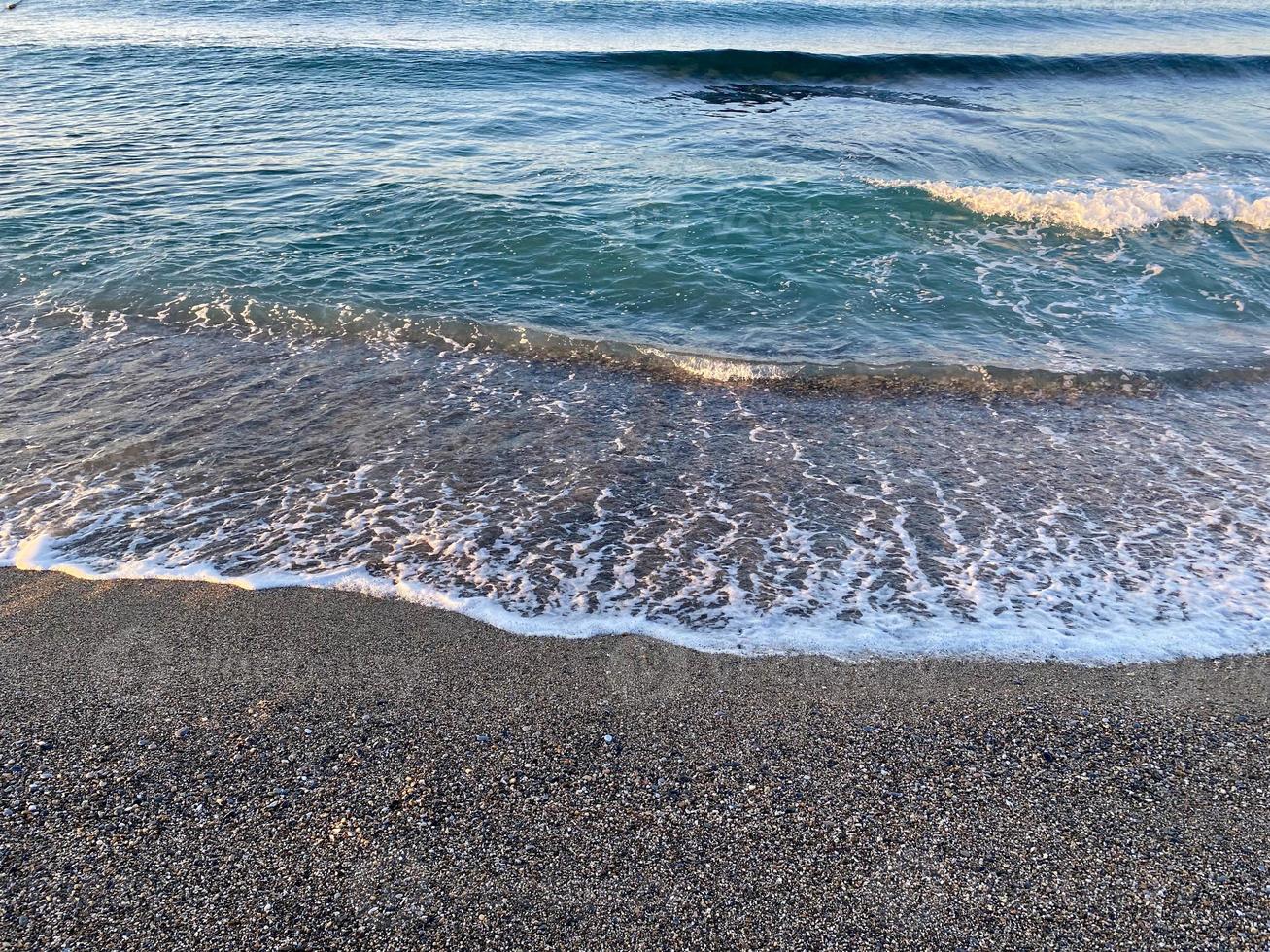Waves of water in the sea and sand with small natural multi-colored stones on the seashore, small pebbles on the beach. Background, texture photo