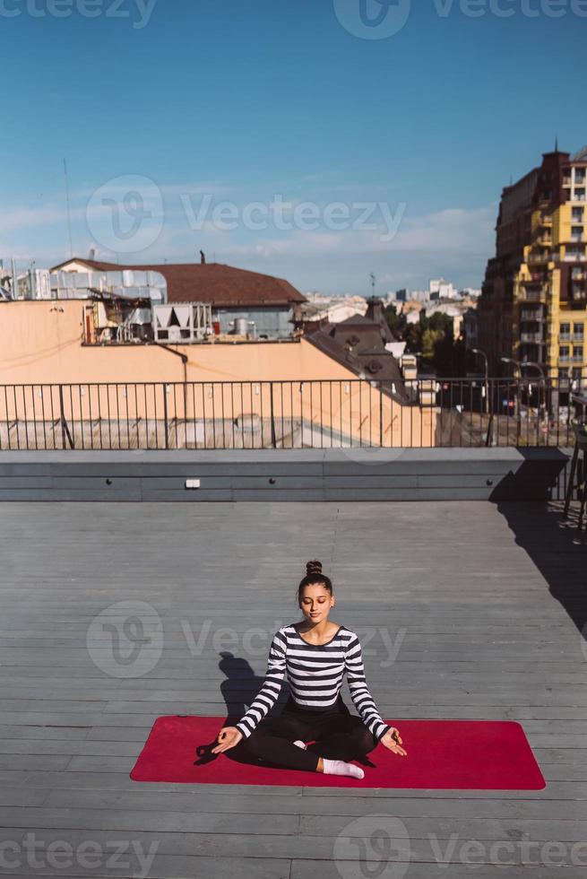 Young woman meditating in lotus pose at roof of the building photo