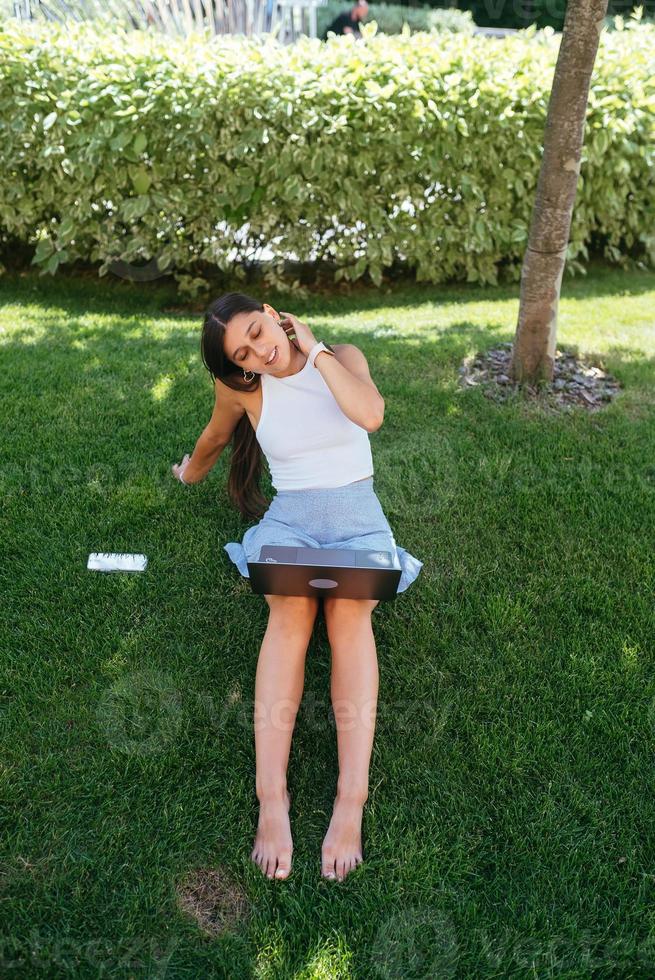 Young girl works with a laptop, sitting on the lawn. photo