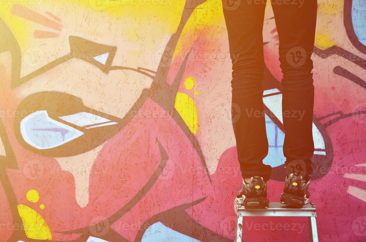 A young graffiti artist paints a new graffiti on the wall. Photo of the process of drawing a graffiti on a wall close-up. The concept of street art and illegal vandalism