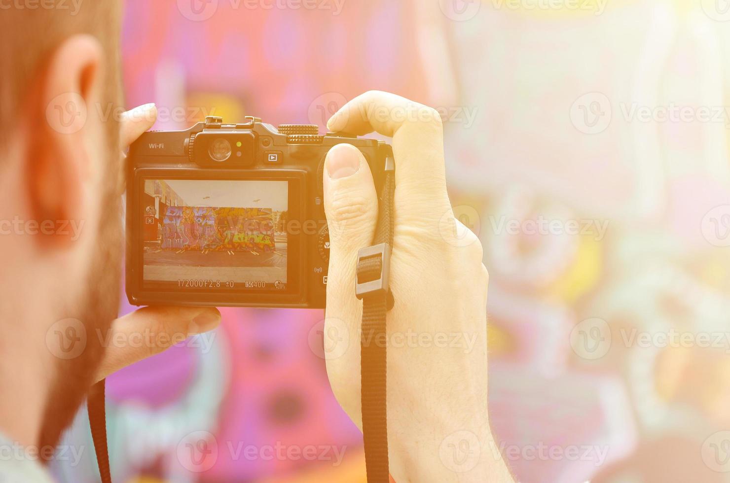 A young graffiti artist photographs his completed picture on the wall. The guy uses modern technology to capture a colorful abstract graffiti drawing. Focus on the photographing device photo