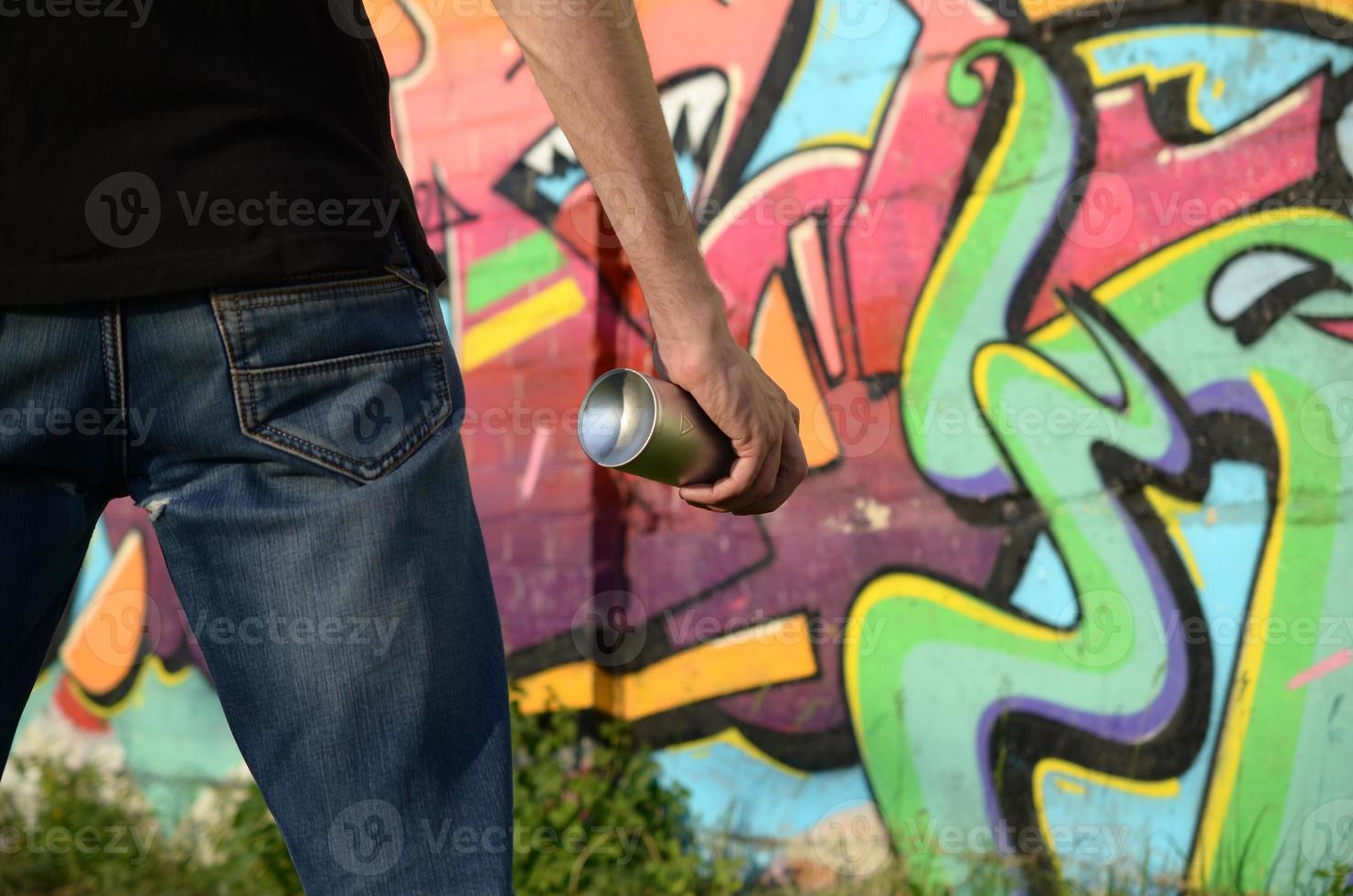 Young graffiti artist with backpack and gas mask on his neck paints colorful graffiti in pink tones on brick wall. Street art and contemporary painting process photo