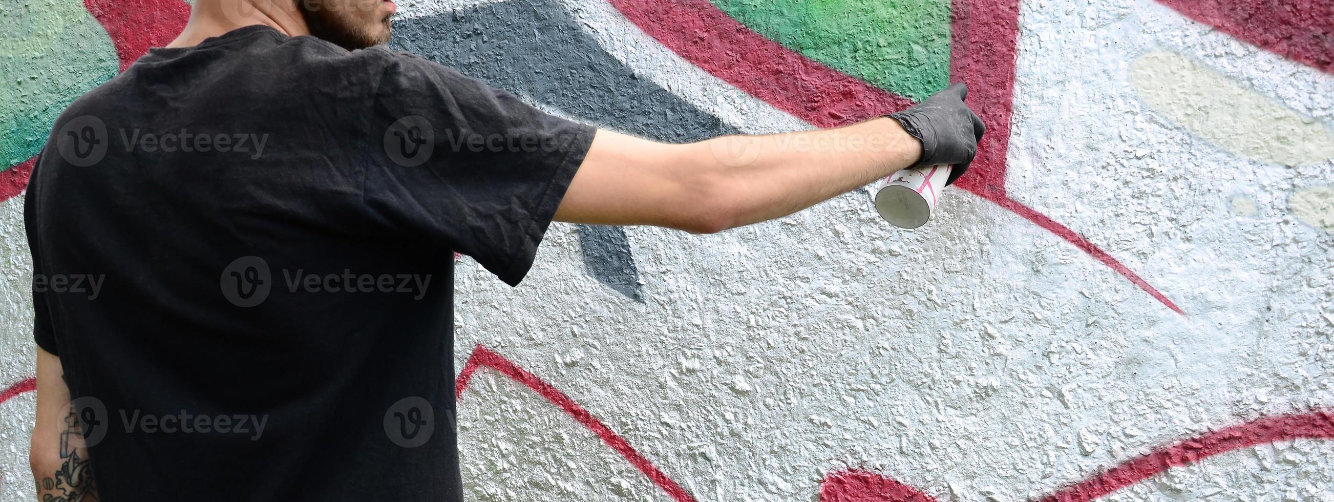 A young hooligan paints graffiti on a concrete wall. Illegal vandalism concept. Street art photo