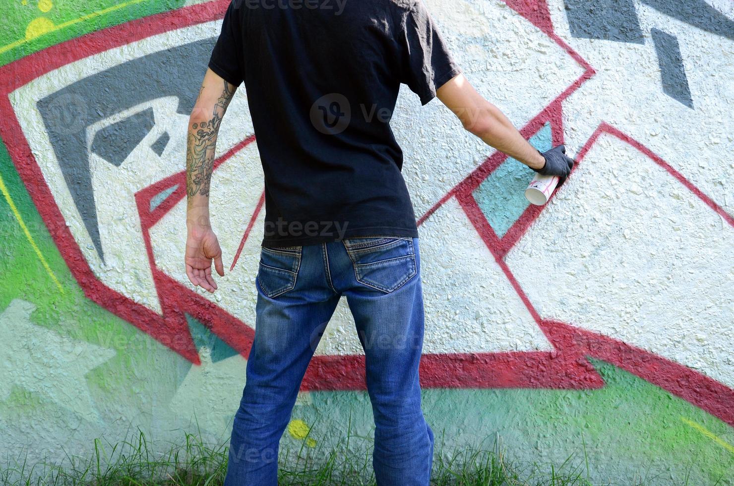 A young hooligan paints graffiti on a concrete wall. Illegal vandalism concept. Street art photo