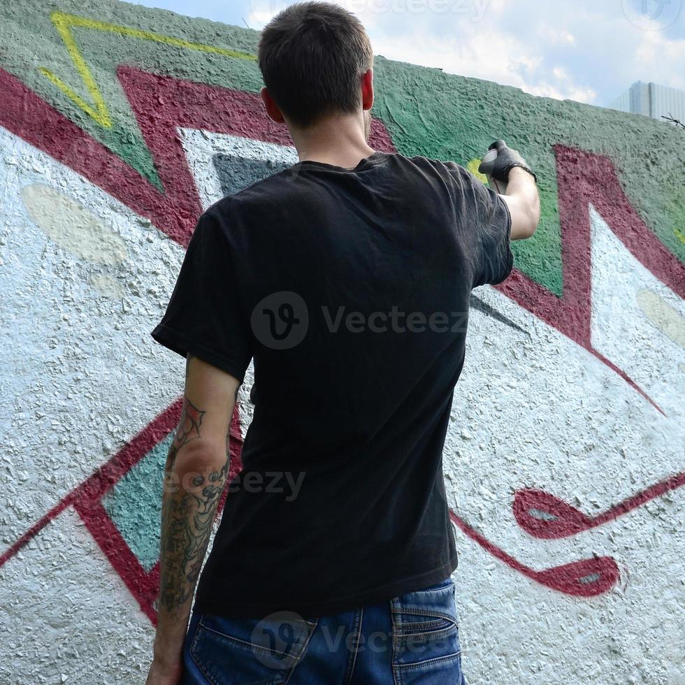 A young hooligan paints graffiti on a concrete wall. Illegal vandalism concept. Street art photo