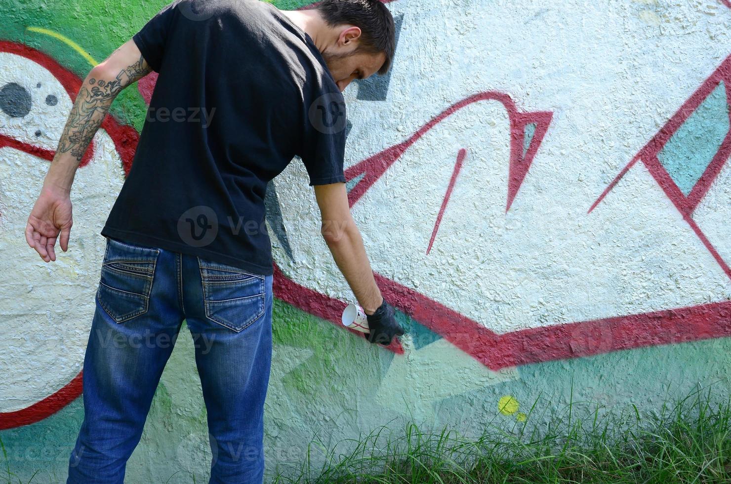 A young hooligan paints graffiti on a concrete wall. Illegal vandalism concept. Street art photo