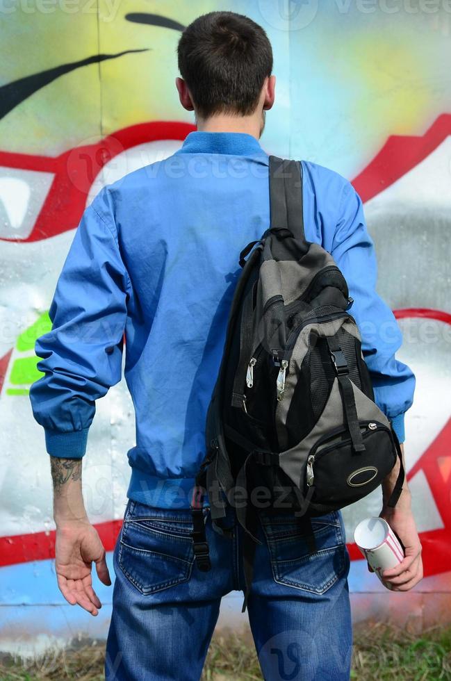 A young graffiti artist with a black bag looks at the wall with his graffiti on a wall. Street art concept photo