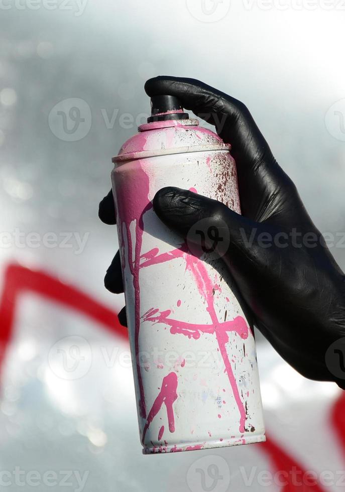 A hand with a spray can that draws a new graffiti on the wall. Photo of the process of drawing a graffiti on a metal wall. The concept of street art and illegal vandalism