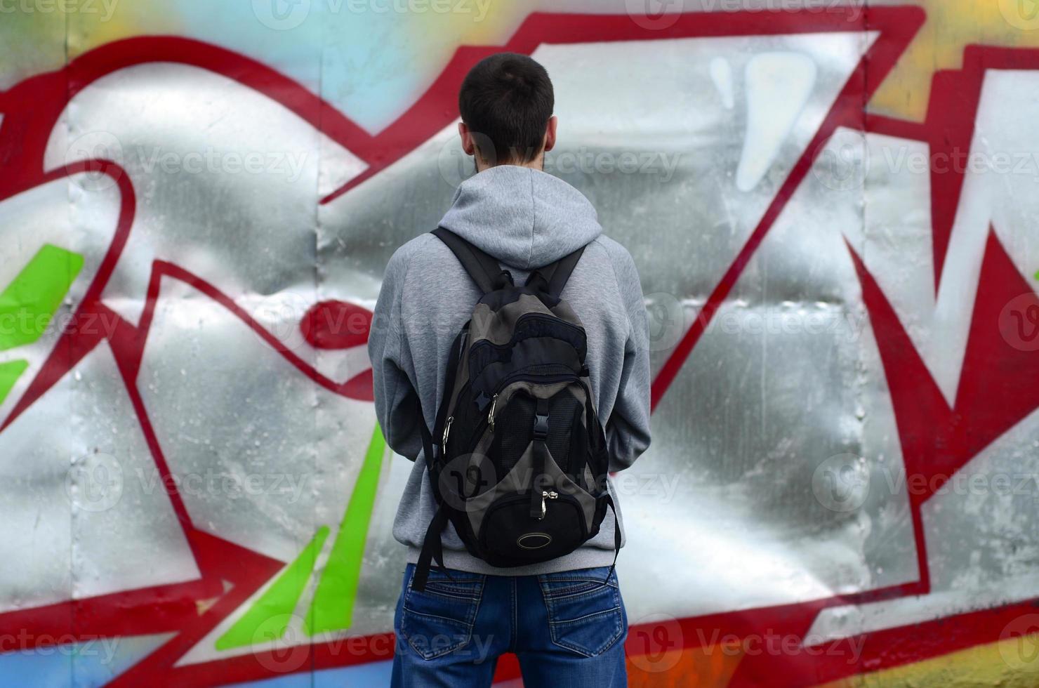 A young graffiti artist with a black bag looks at the wall with his graffiti on a wall. Street art concept photo