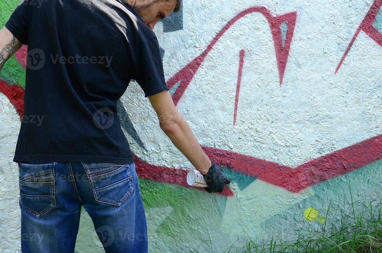 A young hooligan paints graffiti on a concrete wall. Illegal vandalism concept. Street art photo