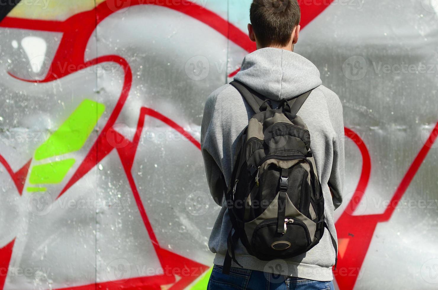 un joven artista de graffiti con una bolsa negra mira la pared con su graffiti en una pared. concepto de arte callejero foto