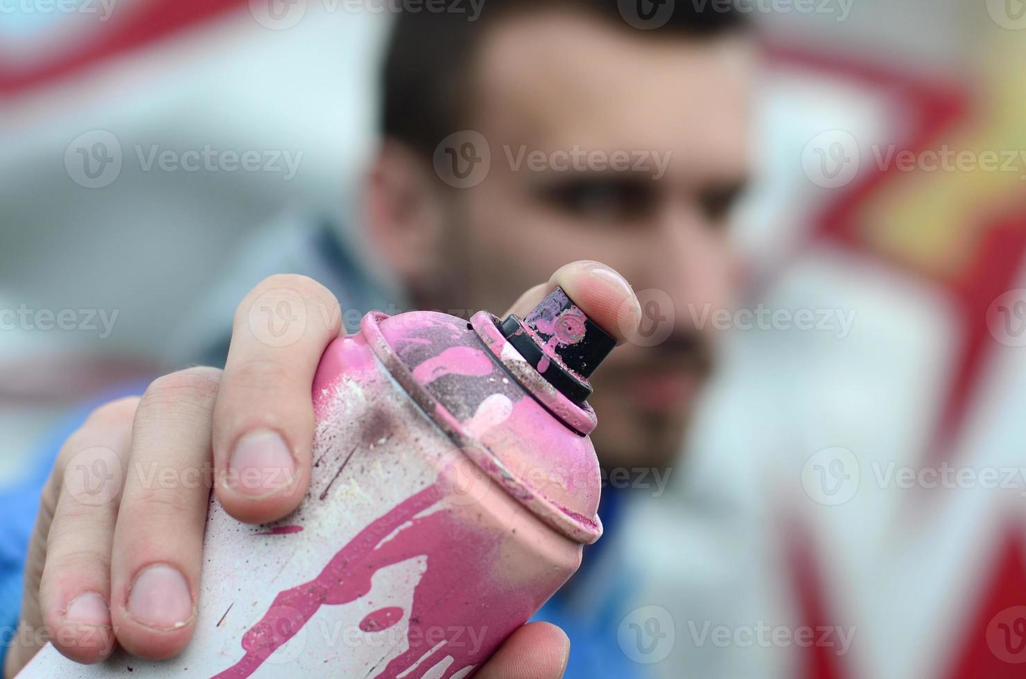 un joven artista de graffiti con una chaqueta azul sostiene una lata de pintura frente a él sobre un fondo de dibujo de graffiti de colores. concepto de arte callejero y vandalismo foto