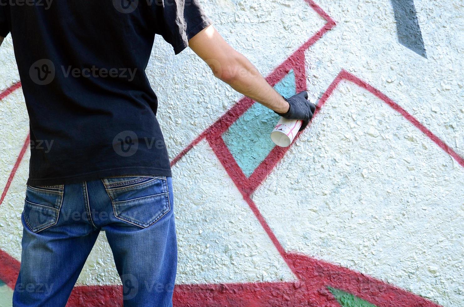 A young hooligan paints graffiti on a concrete wall. Illegal vandalism concept. Street art photo