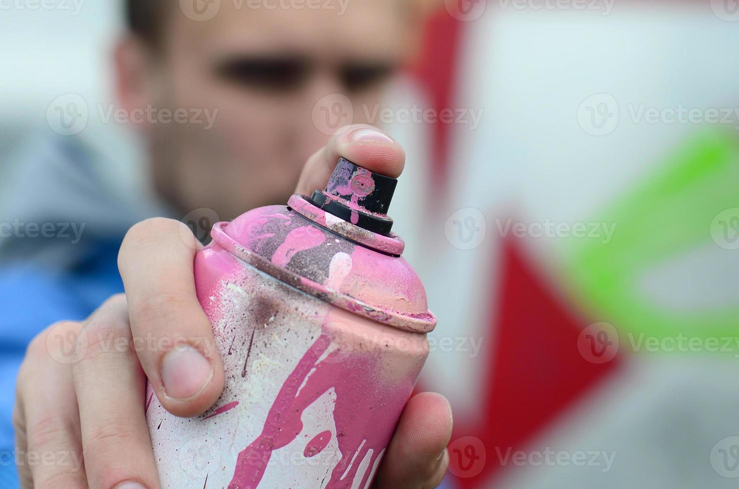 un joven artista de graffiti con una chaqueta azul sostiene una lata de pintura frente a él sobre un fondo de dibujo de graffiti de colores. concepto de arte callejero y vandalismo foto