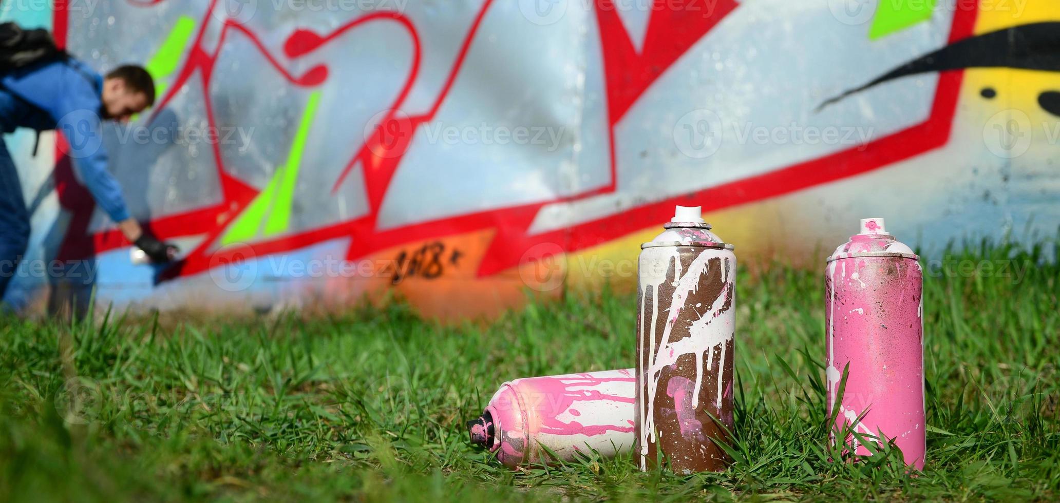 unas cuantas latas de pintura usadas contra el fondo del espacio con la pared en la que el joven dibuja un gran dibujo de graffiti. arte moderno de dibujar paredes en graffiti foto