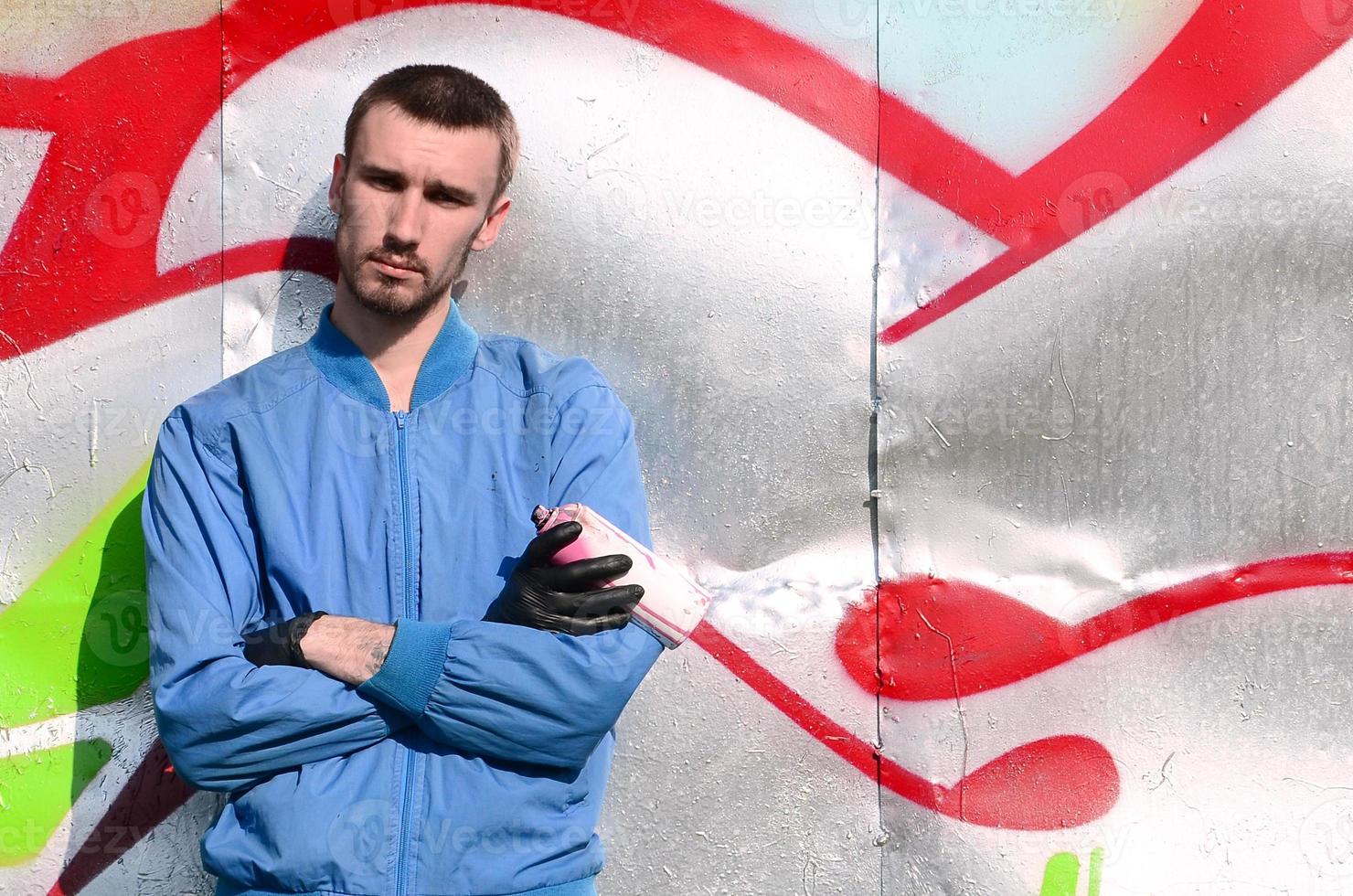 The graffiti artist with spray can poses against the background of a colorful painted wall. Street art concept photo