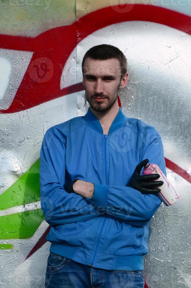 The graffiti artist with spray can poses against the background of a colorful painted wall. Street art concept photo