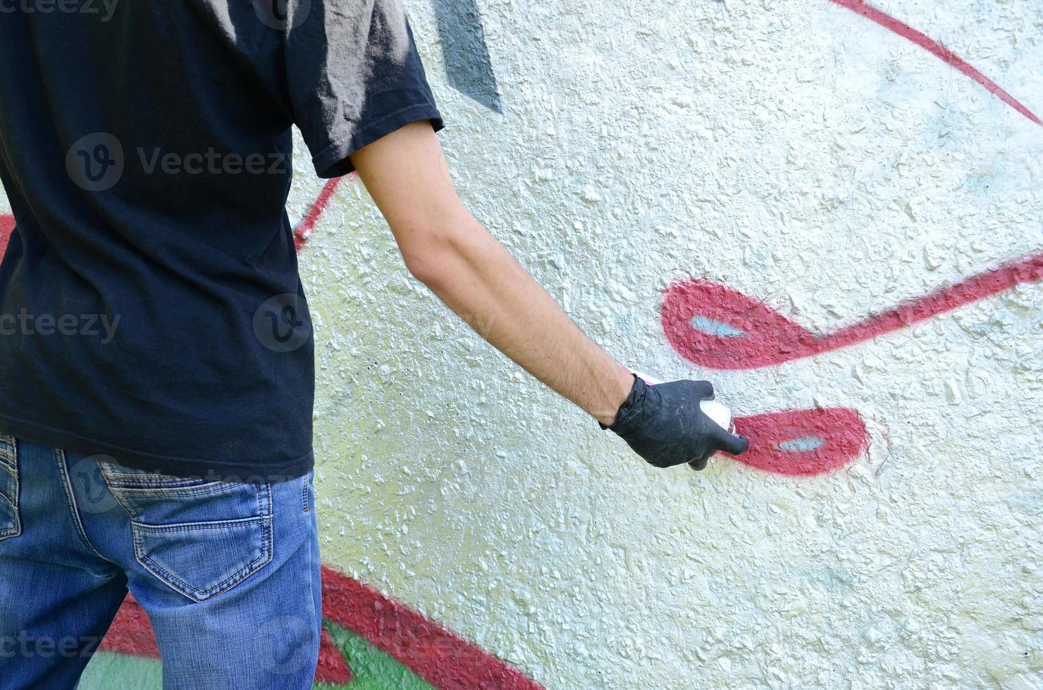 A young hooligan paints graffiti on a concrete wall. Illegal vandalism concept. Street art photo