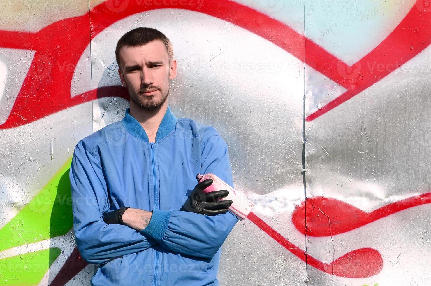 The graffiti artist with spray can poses against the background of a colorful painted wall. Street art concept photo