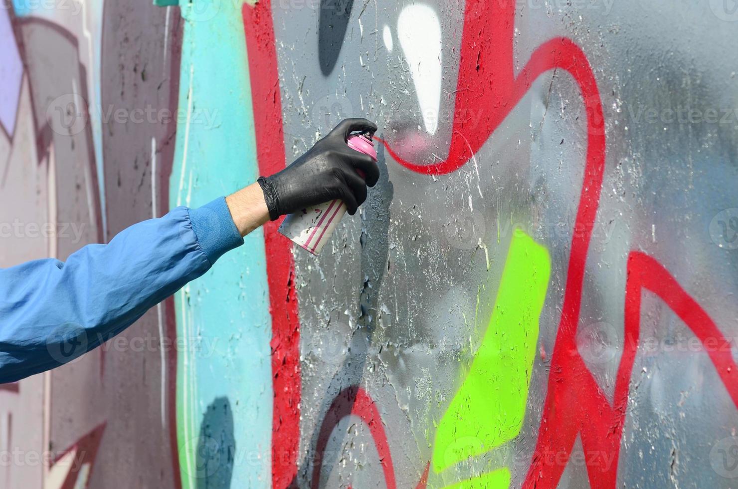 A hand with a spray can that draws a new graffiti on the wall. Photo of the process of drawing a graffiti on a metal wall. The concept of street art and illegal vandalism