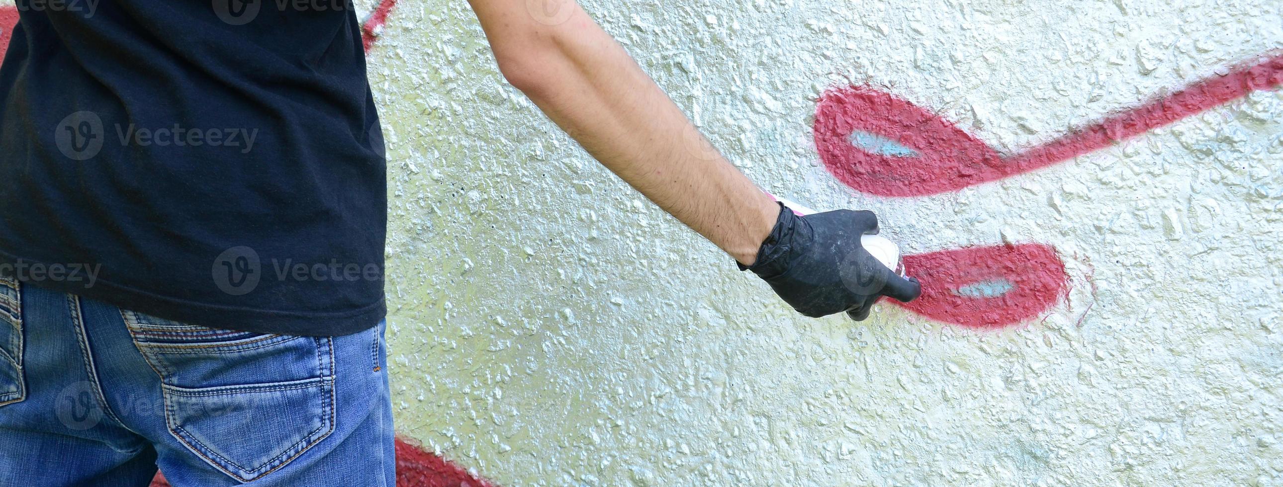 A young hooligan paints graffiti on a concrete wall. Illegal vandalism concept. Street art photo