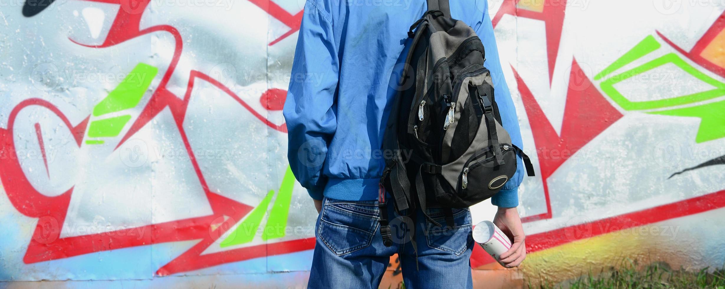 A young graffiti artist with a black bag looks at the wall with his graffiti on a wall. Street art concept photo