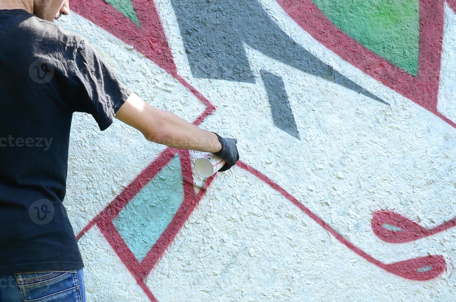 A young hooligan paints graffiti on a concrete wall. Illegal vandalism concept. Street art photo