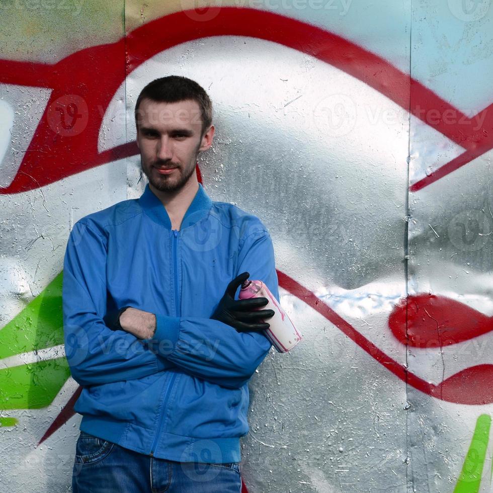 The graffiti artist with spray can poses against the background of a colorful painted wall. Street art concept photo