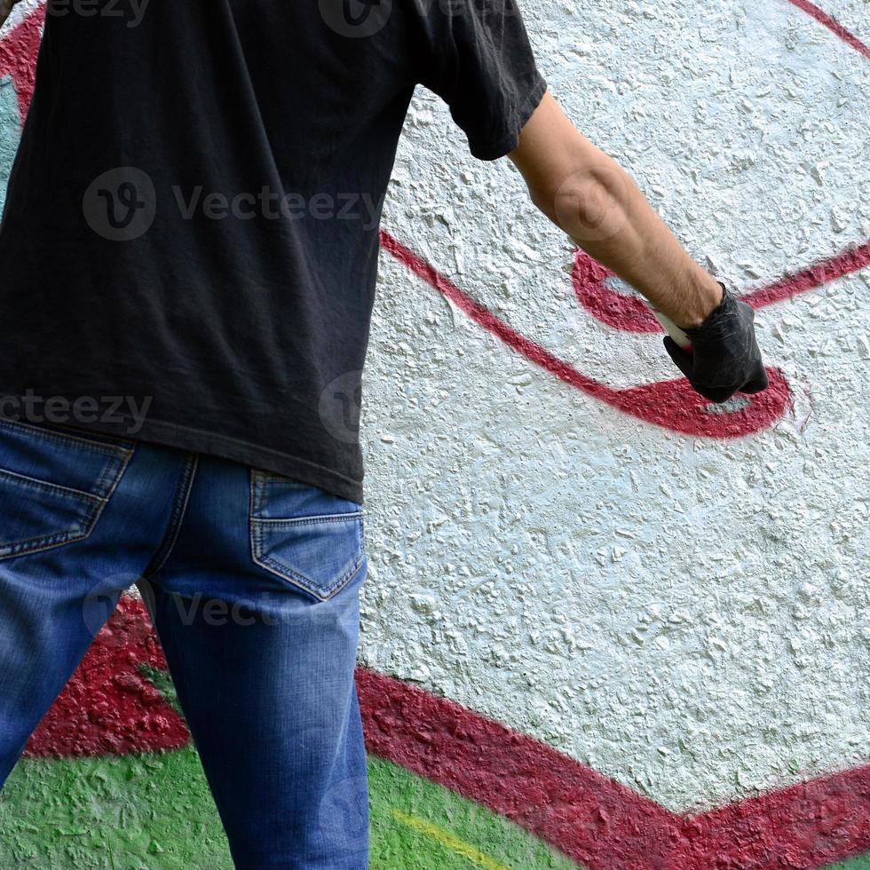 A young hooligan paints graffiti on a concrete wall. Illegal vandalism concept. Street art photo