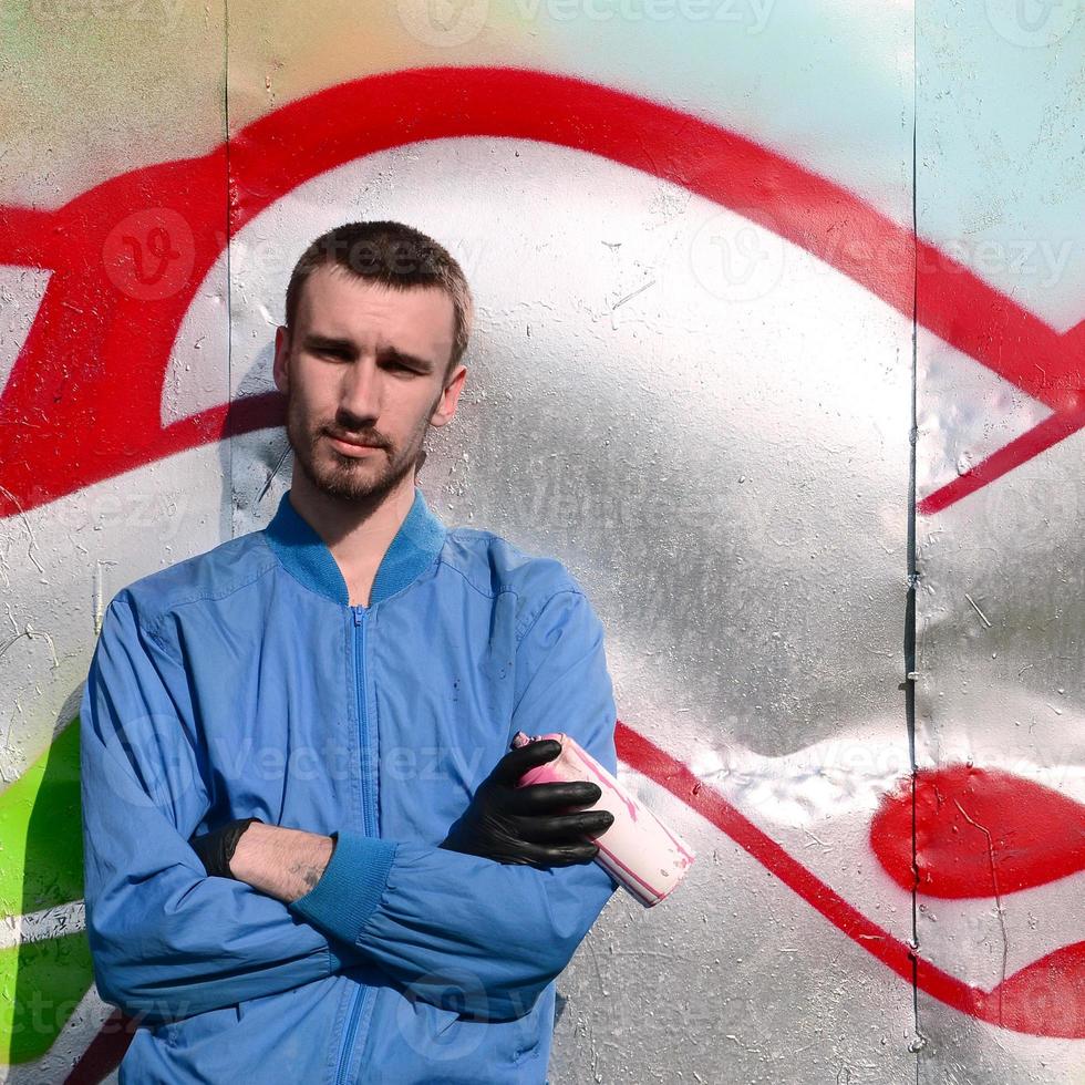 el artista de graffiti con lata de aerosol posa contra el fondo de una pared pintada de colores. concepto de arte callejero foto