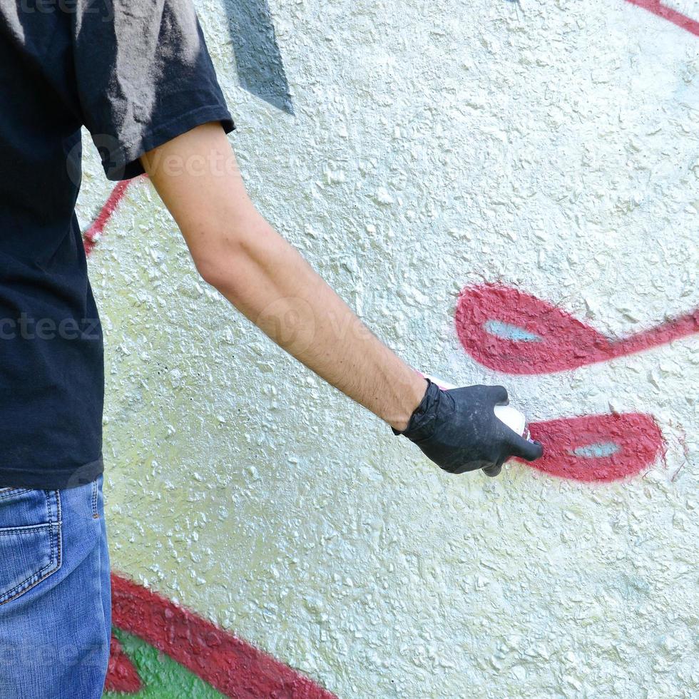 A young hooligan paints graffiti on a concrete wall. Illegal vandalism concept. Street art photo