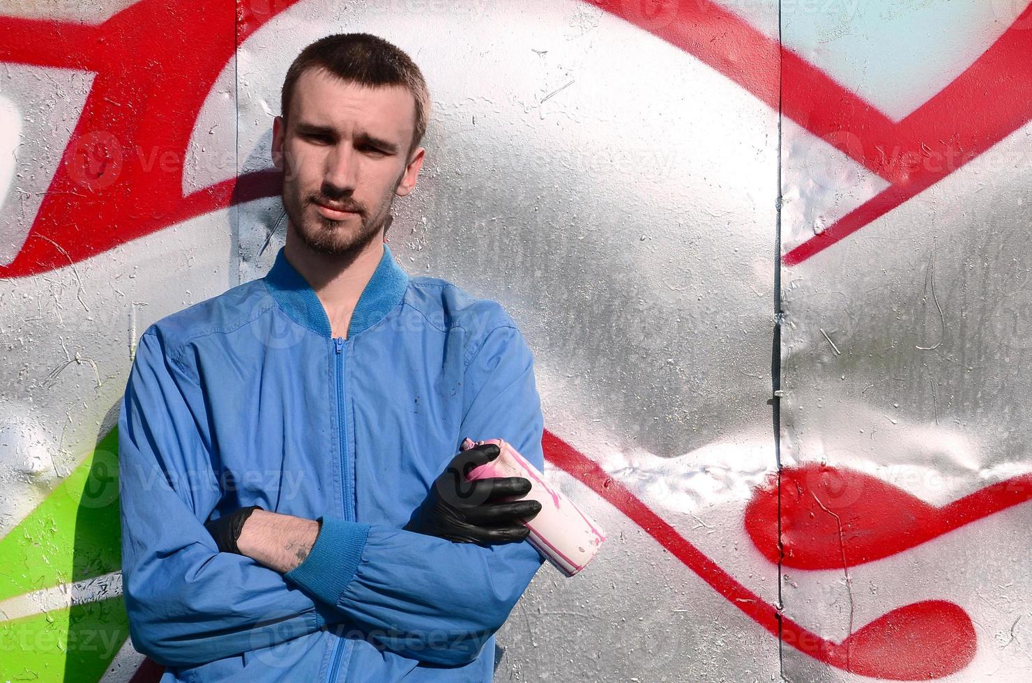 The graffiti artist with spray can poses against the background of a colorful painted wall. Street art concept photo